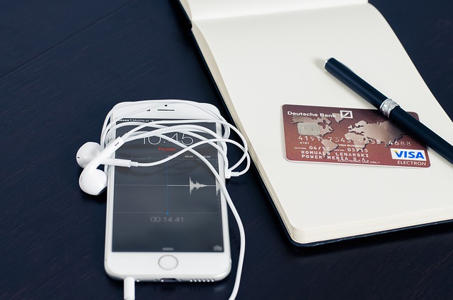 iphone with attached earphone and Visa card beside 